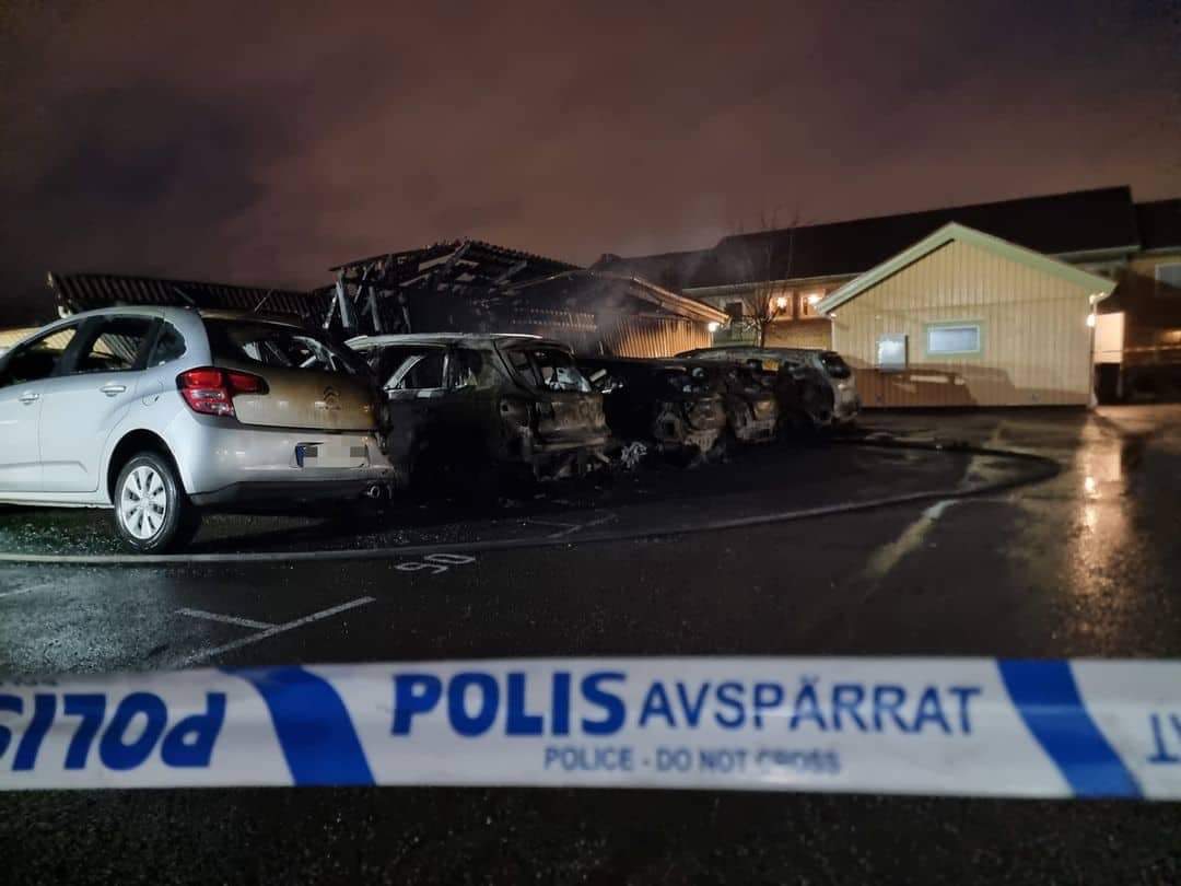 Bilden visar brända bilar bakom polisavspärrning.